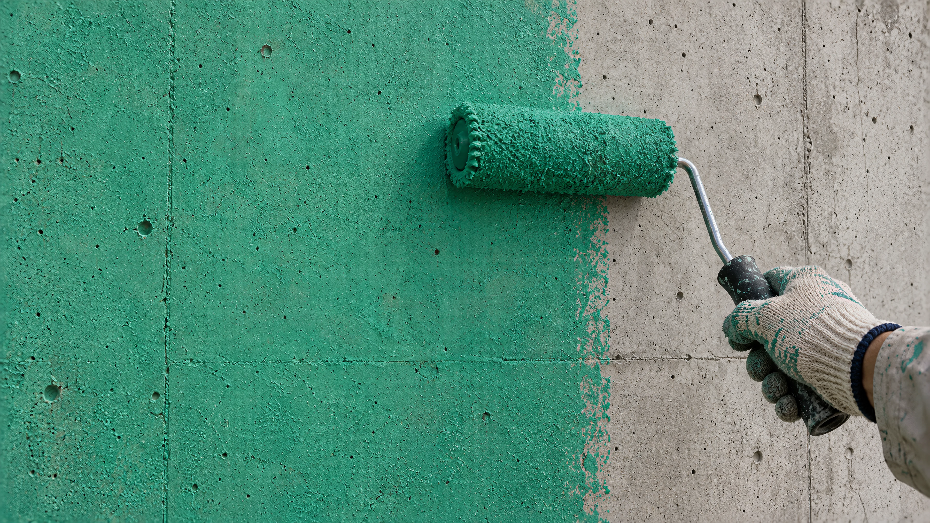 A roller puts the thin green coat on smooth concrete